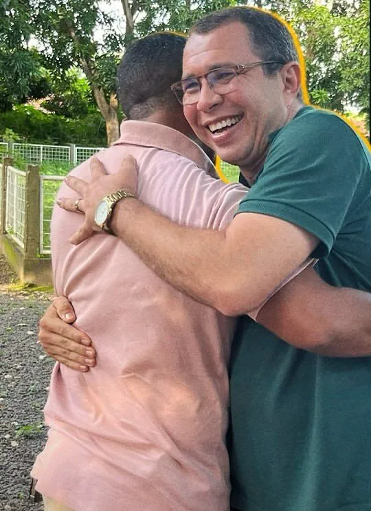 Etniel Anchieta abraçando um apoiador em uma rua arborizada, os dois sorrindo.
