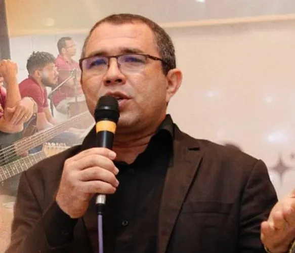 Etniel Anchieta pregando ao microfone, de terno escuro, durante um culto.